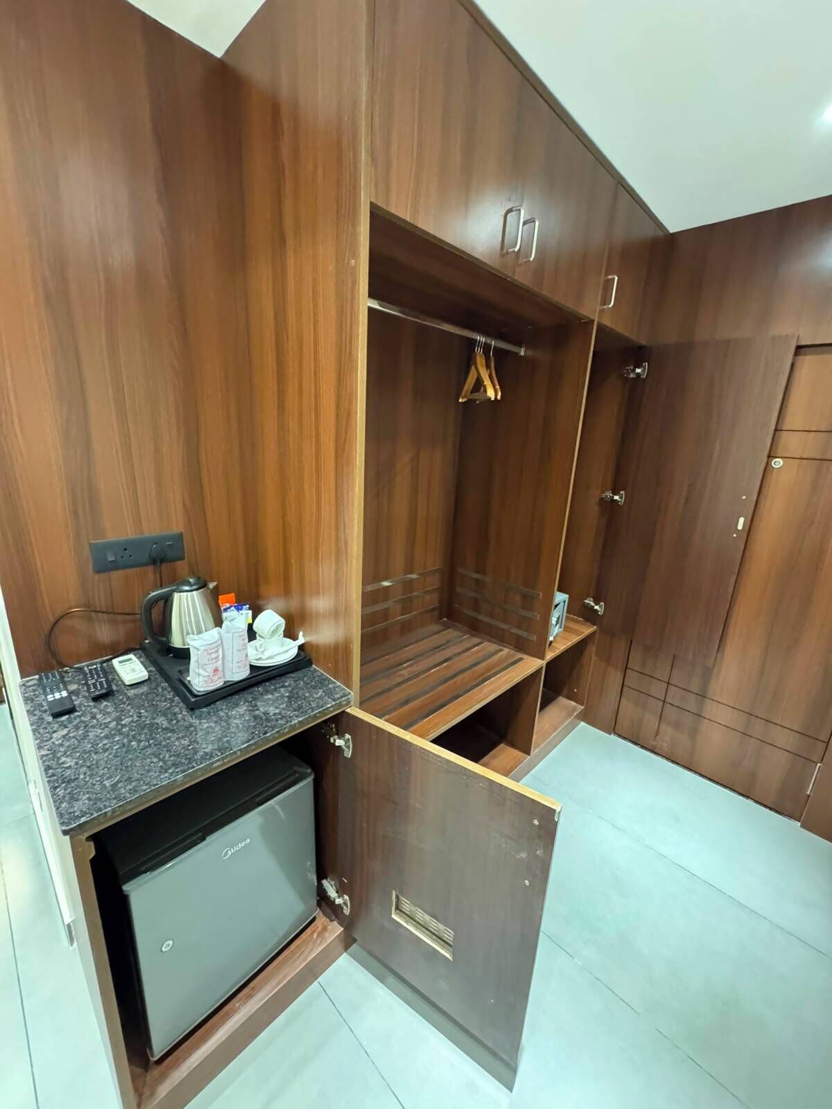 A compact room with a built-in kitchenette, a wardrobe, and a seating area.