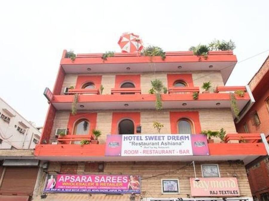Um edifício de vários andares com uma placa para HOTEL SWEET DREAM "Restaurant Ashiana", indicando que oferece quartos, um restaurante e um bar.