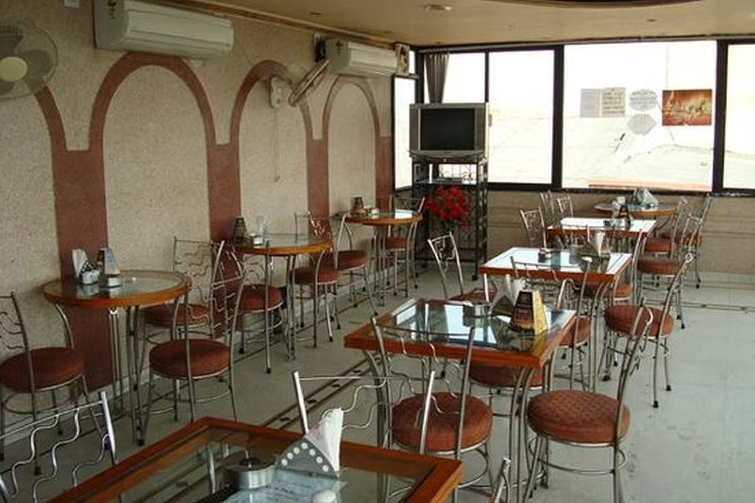 Un restaurante con varias mesas y sillas, un televisor en la pared y ventanas amplias.