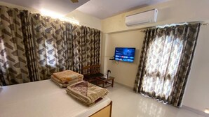 Una habitación de hotel con cama, televisor montado en la pared y cortinas.