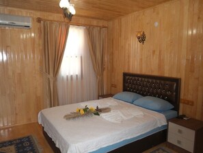 Ein Zimmer mit Holzwandverkleidung, einem Bett, Vorhängen, einem Nachttisch und einer Wandleuchte.