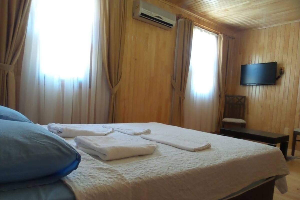 A hotel room with a bed, a flat-screen TV mounted on the wall, and a window with curtains.