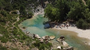 Un paysage naturel avec une rivière aux eaux claires, un terrain rocheux et un groupe de personnes rassemblées près du bord de l’eau.