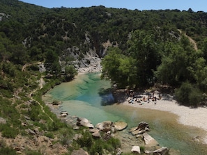 Un paysage naturel avec une rivière aux eaux claires, un terrain rocheux et un groupe de personnes rassemblées près du bord de l’eau.