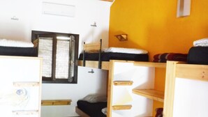 Een compacte kamer met een schuine kap, een raam met zonwering en ingebouwde houten planken.