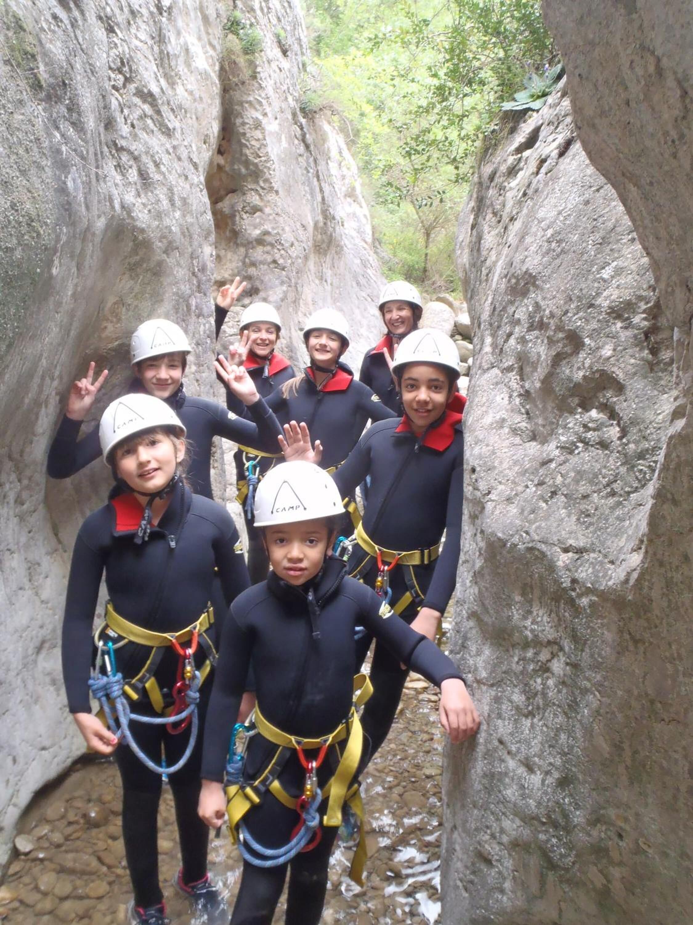 A group of people in a narrow canyon with rocky walls, wearing helmets and harnesses, suggesting a guided outdoor activity.