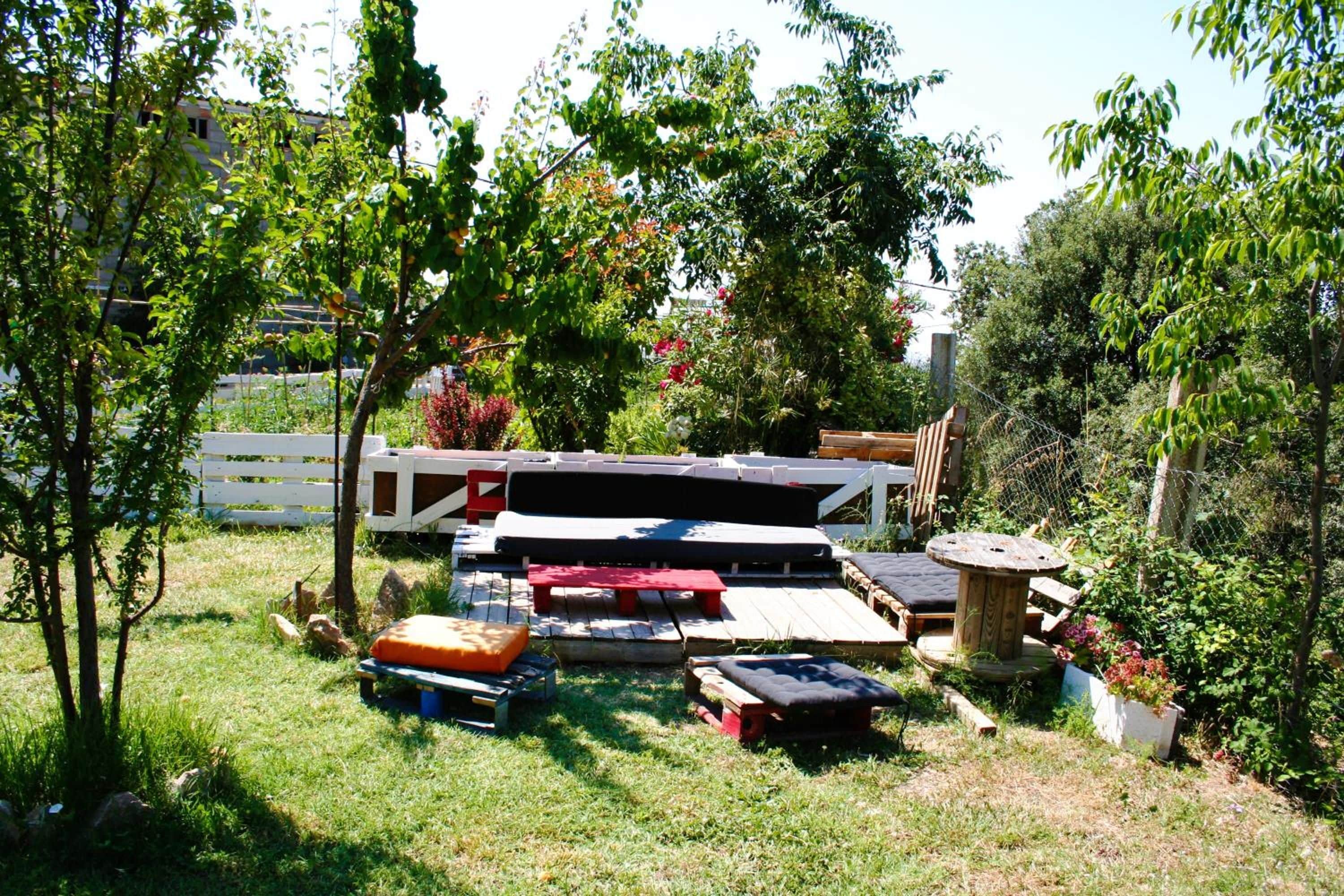 An outdoor seating area with wooden benches and tables, surrounded by greenery and trees.