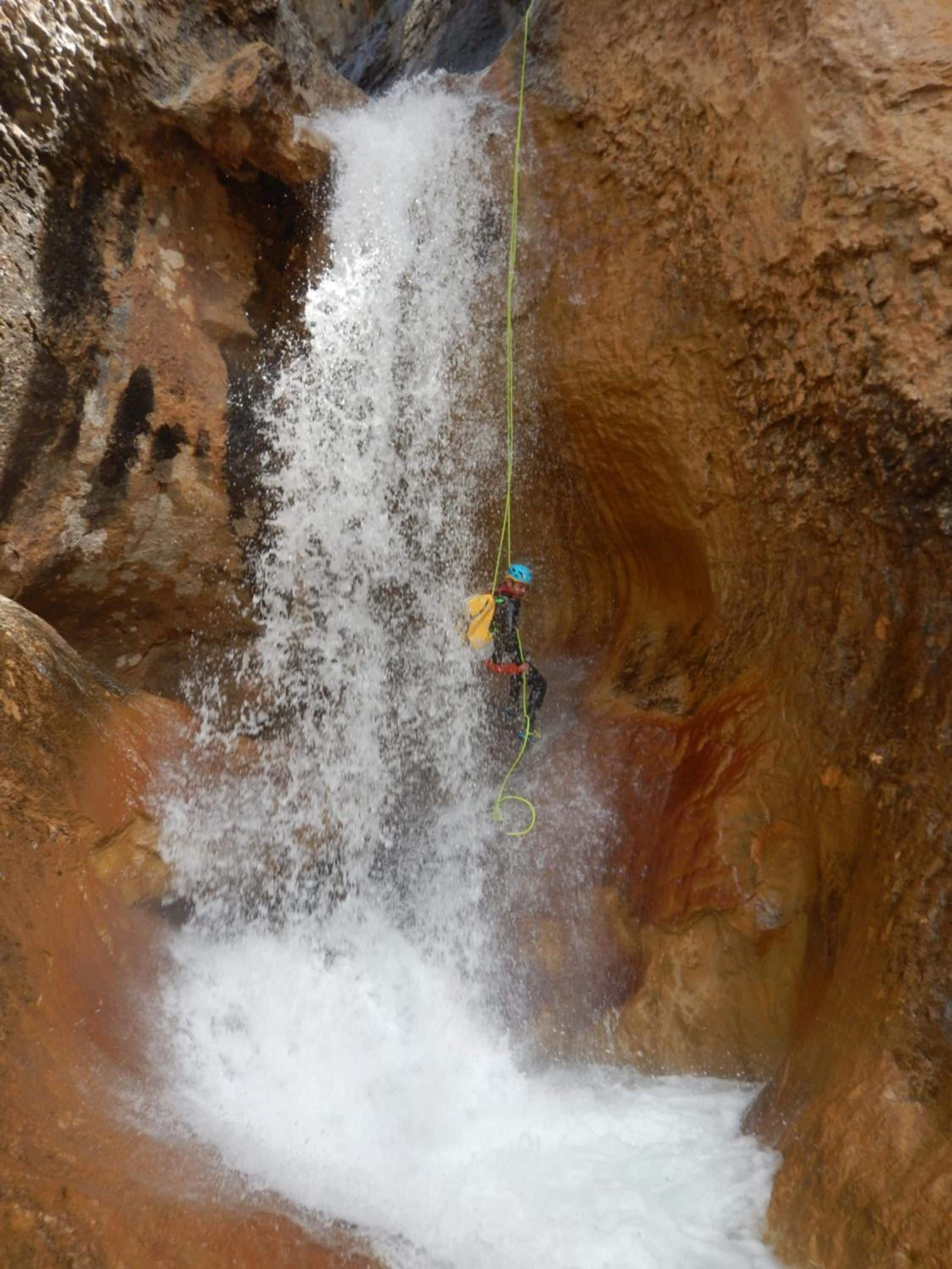 A person rappelling down a waterfall in a rocky gorge.