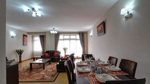 A dining area with a table set for four, a sofa, and a coffee table in the foreground. - Fenesi Gardens Apartments (Nairobi)
