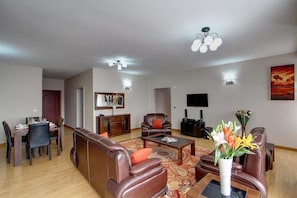A spacious living room with a dining area, leather sofas, a coffee table, and a flat-screen TV. - Fenesi Gardens Apartments (Nairobi)