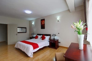A hotel room with a bed, bedside tables, a nightstand, a vase with flowers, and a door. - Fenesi Gardens Apartments (Nairobi)