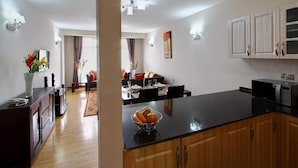 A modern kitchen with a black countertop, wooden cabinets, and a dining area with a table and chairs. - Fenesi Gardens Apartments (Nairobi)