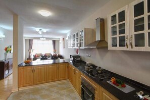 A modern kitchen with wooden cabinets, a black countertop, and a central island. - Fenesi Gardens Apartments (Nairobi)