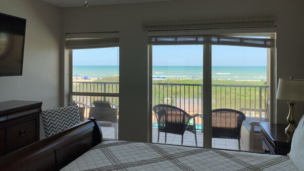 A bedroom with a bed, a TV, a ceiling fan, and a view of the beach through large windows. - Beachfront, Luxurious, Great Location with Amazing Views!!! (South Padre Island)