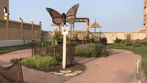A garden pathway with a butterfly sculpture, surrounded by greenery and a wooden fence. - Beachfront, Luxurious, Great Location with Amazing Views!!! (South Padre Island)