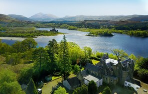 A large, historic building with multiple wings and a courtyard, surrounded by lush greenery and a lake. - Kilchurn Suites (Dalmally)