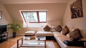 A modern living room with a sofa, a glass coffee table, a television, and a large window. - Kilchurn Suites (Dalmally)