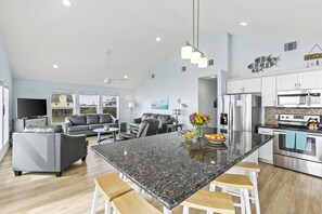 Una cocina moderna con una isla grande, electrodomésticos de acero inoxidable y un comedor con un sofá gris y taburetes de madera.