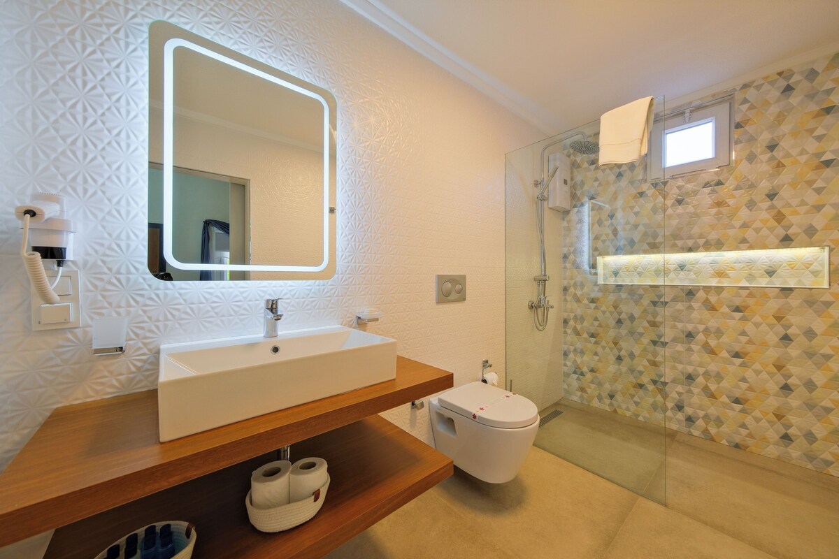 A modern bathroom with a large mirror, a white sink, a toilet, and a shower area.