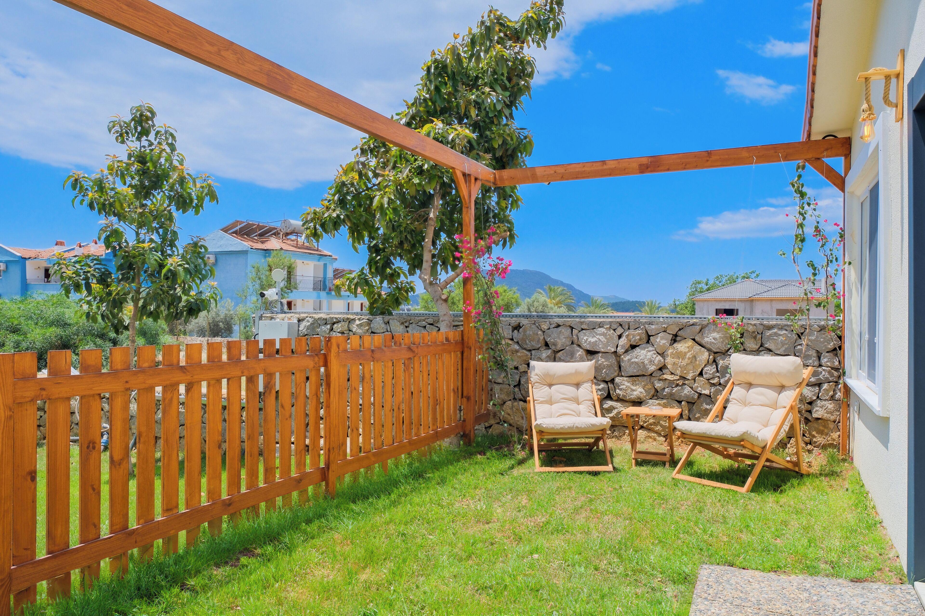 Un patio techado con valla de madera, dos sillas acolchadas y un muro de piedra.