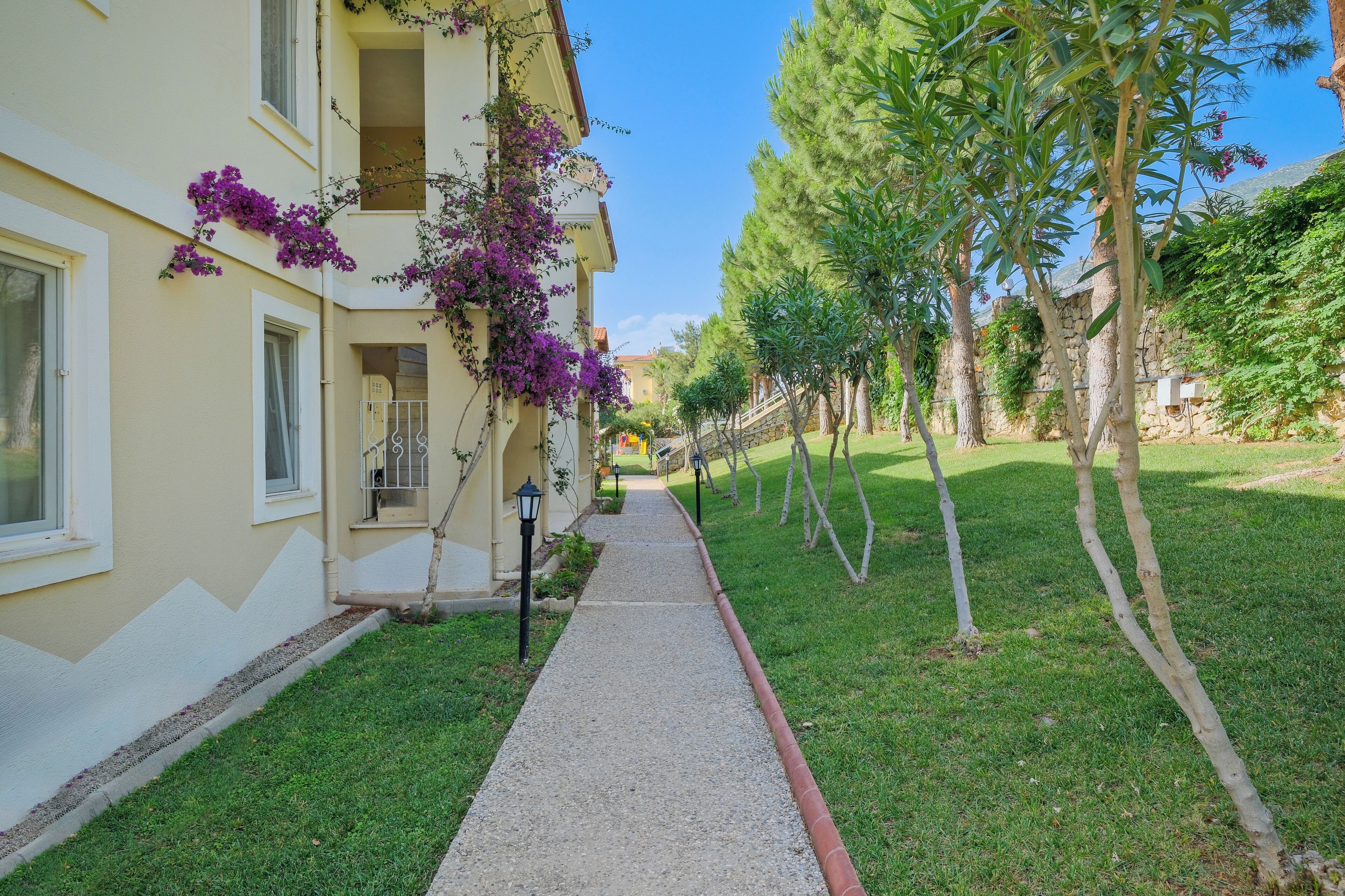 A pathway leading to a building with a balcony, surrounded by trees and a well-maintained lawn.