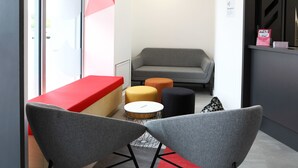 Un área de recepción moderna con un mostrador rojo, sillas grises y un sofá gris.