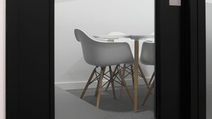 Un espacio de trabajo con pared blanca, puerta de vidrio y una mesa con sillas.