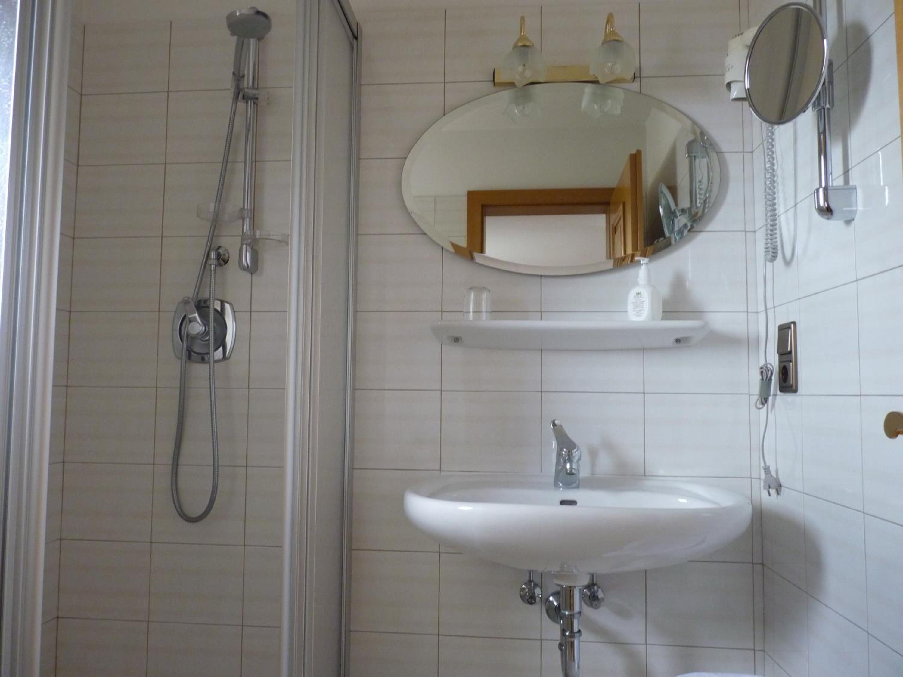 Kylpyhuone, jossa on suihku, pesuallas, peili ja hylly, jossa on hygieniatuotteita.