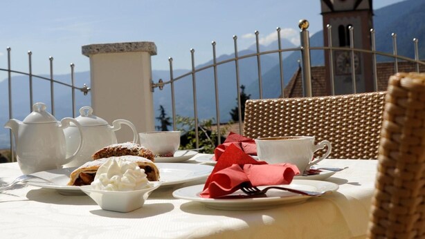 A table set for a meal with a view of a clock tower and mountains in the background. - Hotel Mair am Turm (Tirolo)