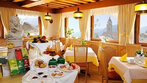 A dining area with wooden furniture, a statue, and a table set with breakfast items. - Hotel Mair am Turm (Tirolo)