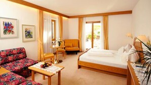 A hotel room with a bed, a sofa, a table with fruit, and two chairs. - Hotel Mair am Turm (Tirolo)