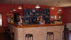 Una zona de bar con mostrador de ladrillo, varios taburetes, luces colgantes y estantes llenos de botellas.