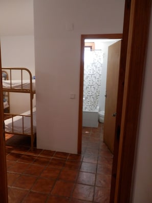 Un couloir étroit, avec un lit superposé sur la gauche et une salle de bain dont on aperçoit les toilettes et la douche au fond.