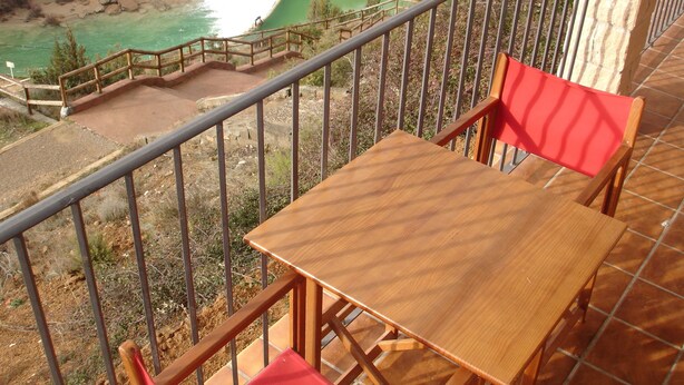 Un balcón con una mesa de madera y sillas rojas con vistas a un paisaje natural que incluye una cascada.