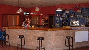 Zona de bar con mostrador de ladrillo, tres taburetes, luces colgantes y una variedad de botellas y una máquina de café.