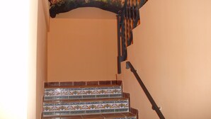 Una escalera con baldosas estampadas, barandilla de metal y una ventana en lo alto.