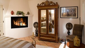 A bedroom with a fireplace, a large wooden cabinet, two floor lamps, a patterned armchair, and a bed with striped bedding. - Experience West Beach living, just steps away from Santa Barbara Harbor (Santa Barbara)