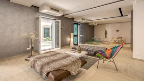 A modern hotel room with a large bed, a sofa, and a colorful chair. There is a window with a view of the outside. - Aurelia Vatican Suites (Rome)