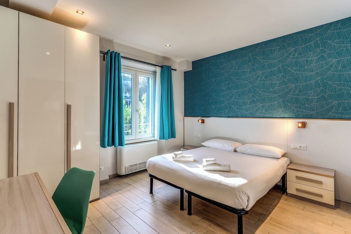 A modern bedroom with a bed, bedside tables, a desk, and a window with curtains.