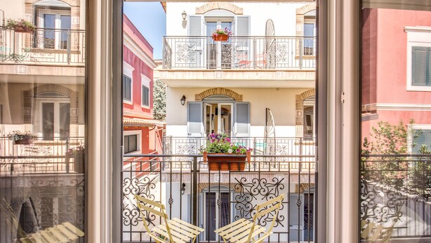 A balcony with two chairs, a potted plant, and a view of neighboring buildings. - Aurelia Vatican Suites (Rome)