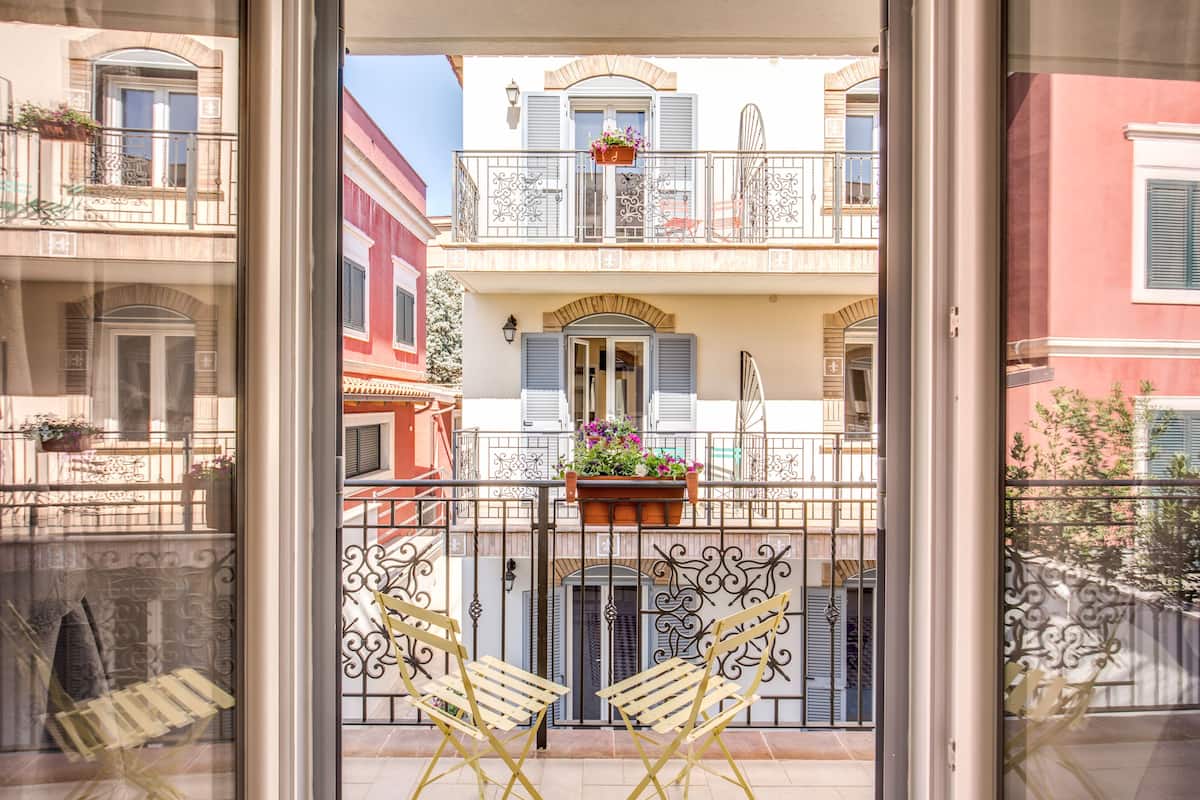 A balcony with two chairs, a potted plant, and a view of neighboring buildings.