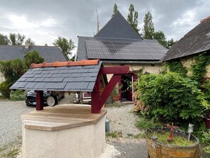A house with a sloped roof, a wooden deck, and a garden area with plants and a barrel. - La Malcotais (Noyal-Chatillon-sur-Seiche)