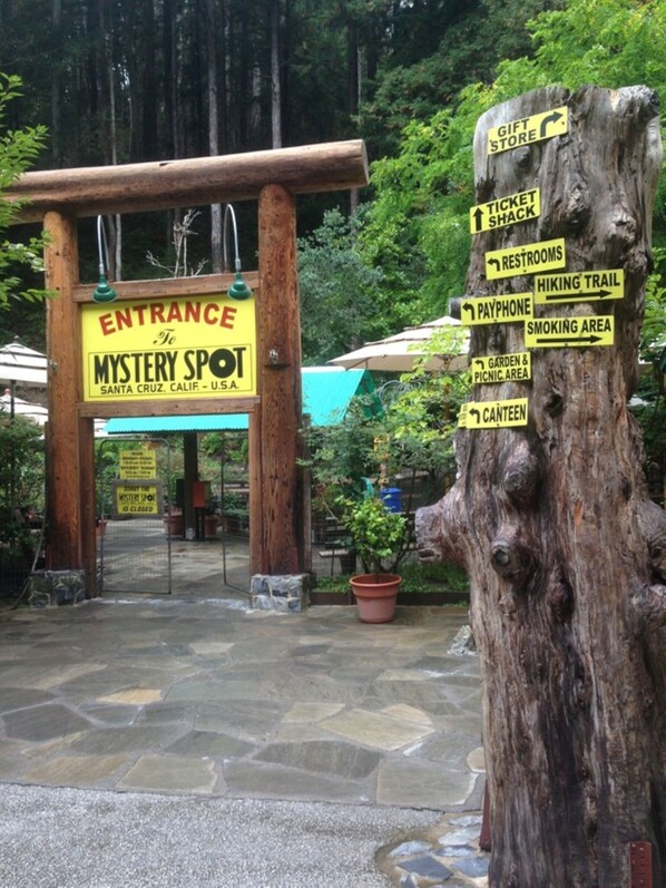En entréskylt för Mystery Spot med vägbeskrivningar till olika faciliteter, som till exempel souvenirbutiken, biljettkiosken, toaletterna, en telefonkiosk, ett område för rökning, en trädgård och en picknickplats samt ett serveringsställe.