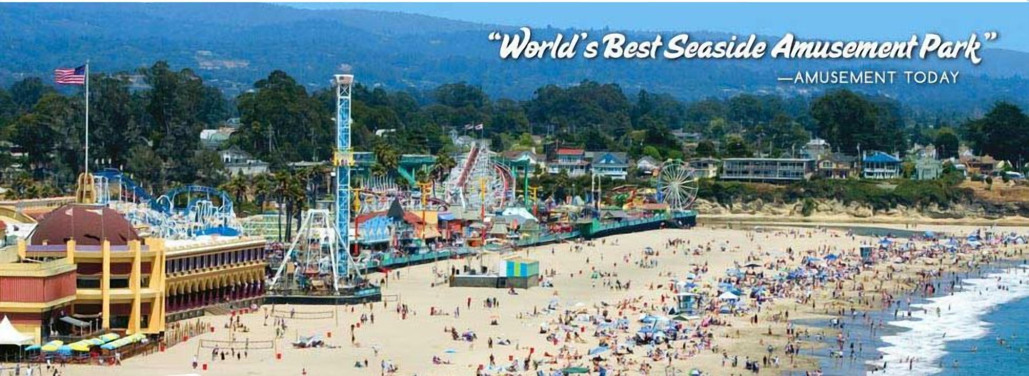 Un parc d’attractions situé en bord de mer, avec une grande roue, des montagnes russes et une promenade en bord de plage.