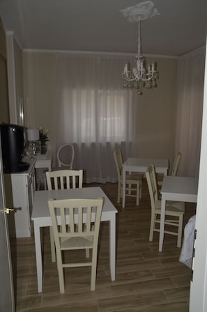 A dining area with a chandelier, white furniture, and a television on a stand. - Operà B&B (Sirolo)