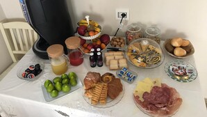 Una mesa con diversos alimentos, como frutas, quesos y embutidos, además de una cafetera.