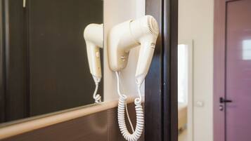 A hair dryer mounted on a wall with a coiled cord.