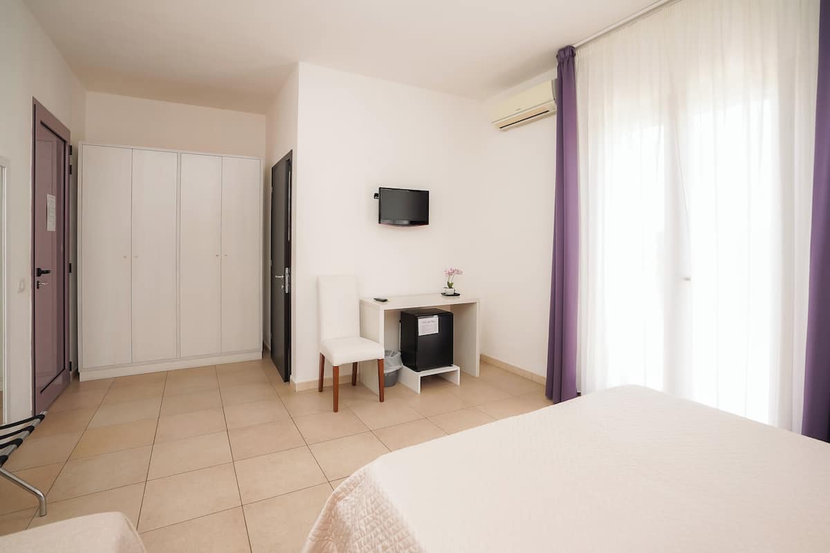 Une chambre d’hôtel avec un lit, un bureau équipé d’un ordinateur, une chaise, une armoire et un téléviseur fixé au mur.