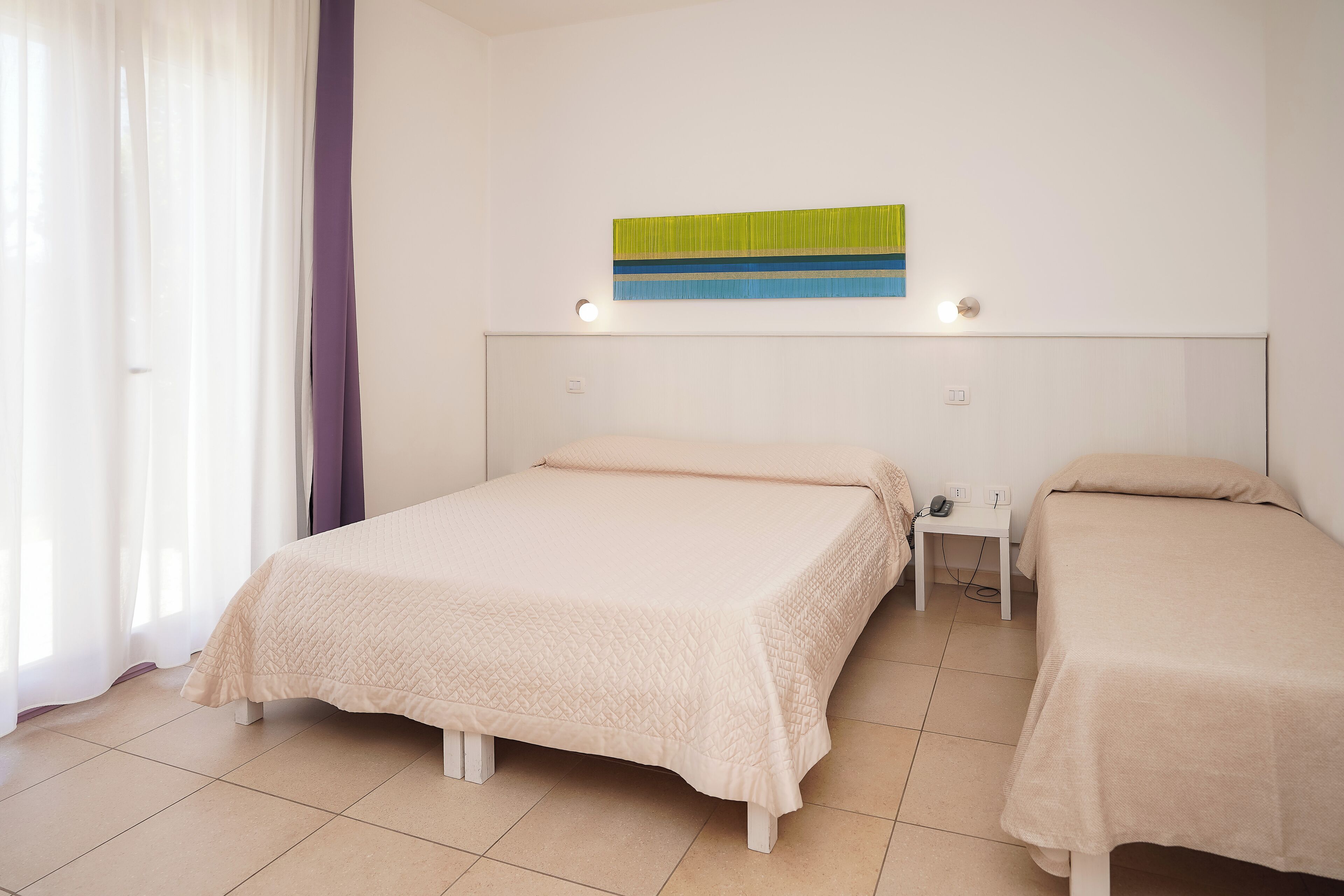A hotel room with two beds, a nightstand, and a wall-mounted light fixture.