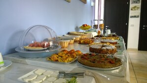 Una mesa de buffet con diversos alimentos, incluyendo pasteles, frutas y un plato de carne tapado.